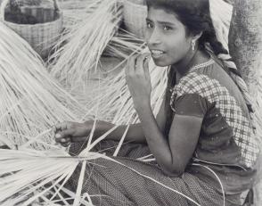 Straw weavers. A girl weaves a raincoat, from Amero Picture Book