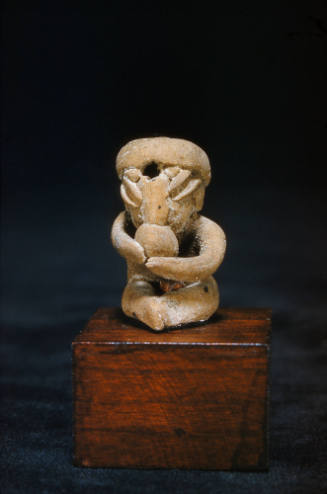 Seated figure holding round object to mouth